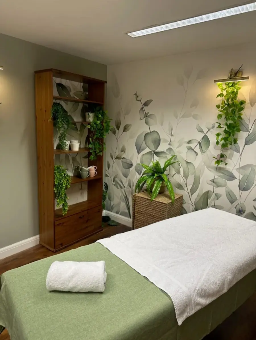 Lucy's treatment room: a massage couch dressed in sage and white towels beside a eucalyptus mural
